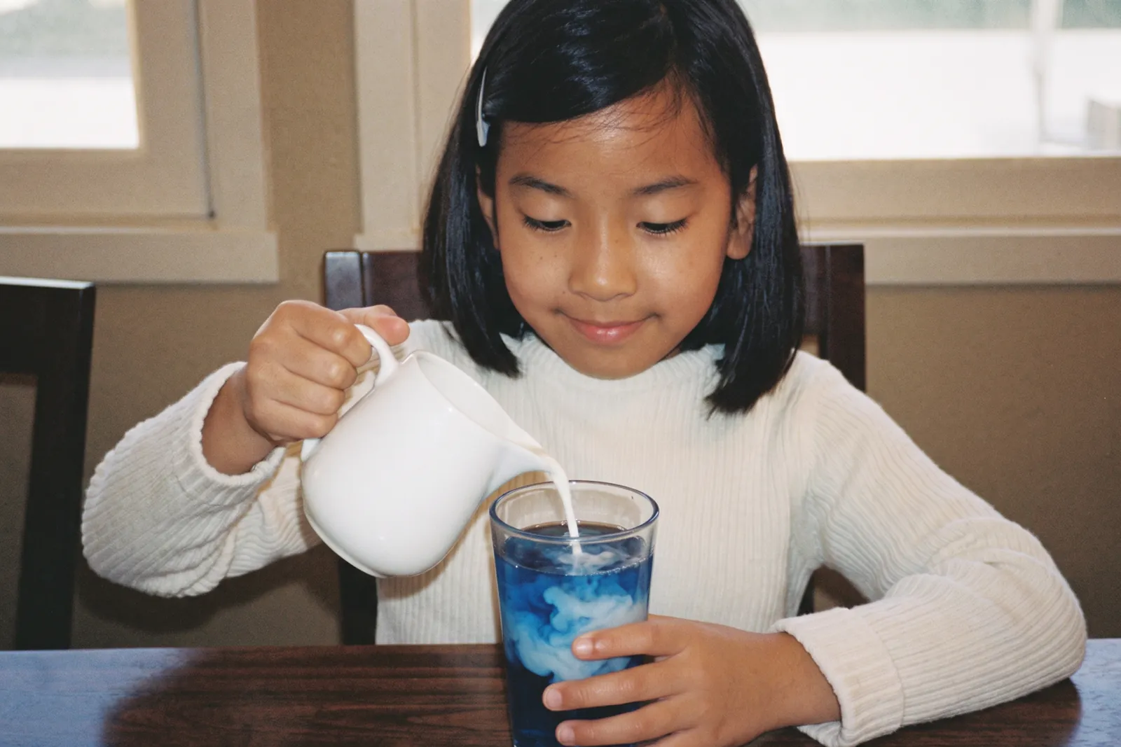 青いお茶にミルクをそっと注ぐ女の子