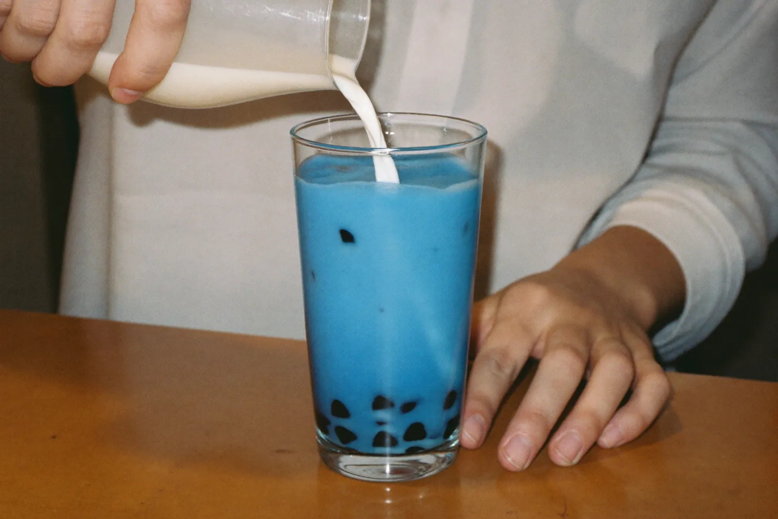 青いお茶にミルクをそっと注ぐ手元