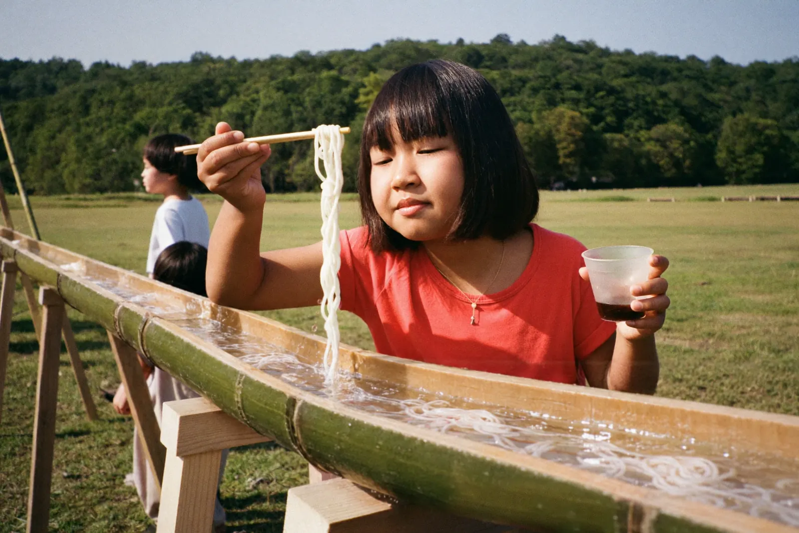 竹のコースを流れるそうめんを箸でつかむ女の子