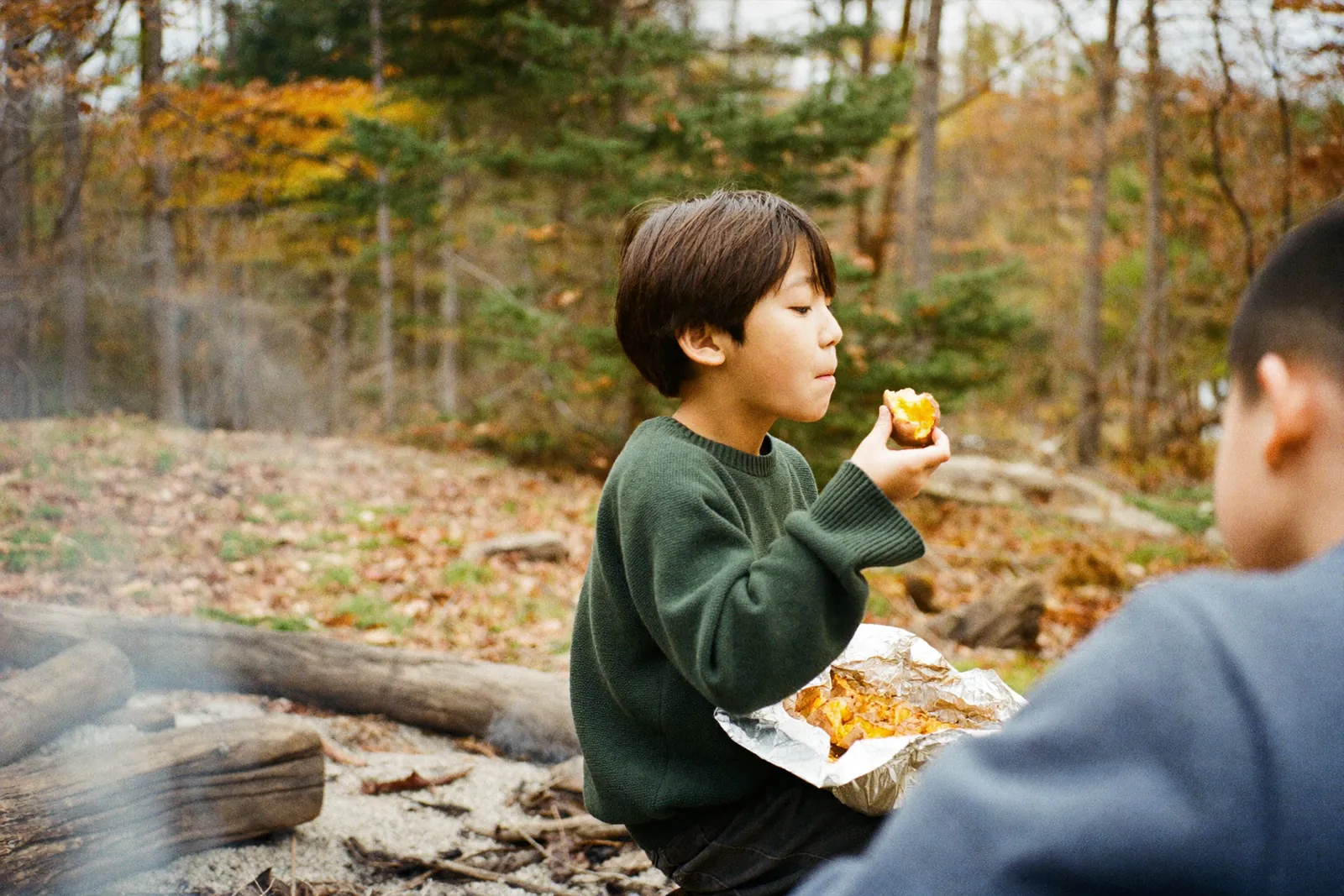 焚き火のそばで焼き芋を食べる男の子