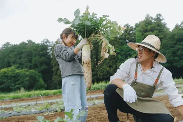 畑で大根を抜いて、農家さんと笑う子ども